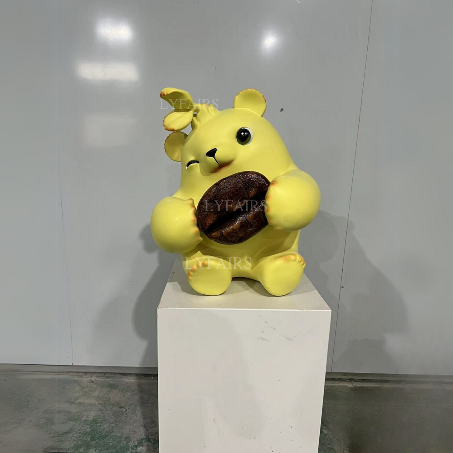 Adorable sculpture d'ours jaune tenant des grains de café